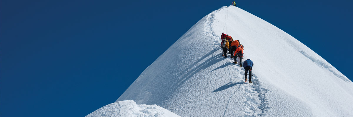 Grupo de escaladores ascendiendo una empinada cumbre nevada bajo un cielo azul claro, simbolizando determinación y trabajo en equipo en el montañismo