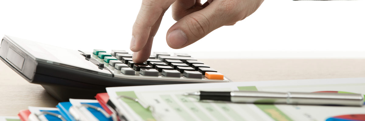 Cálculo de Impuestos Mano presionando un botón en una calculadora junto a documentos impresos con datos numéricos y gráficos circulares, sugiriendo cálculos financieros o análisis de datos estadísticos.