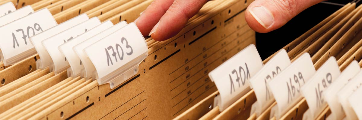 Archivo de expedientes numerados Mano revisando fichas de archivo numeradas en cajón de expedientes, gestión documental y organización administrativa.