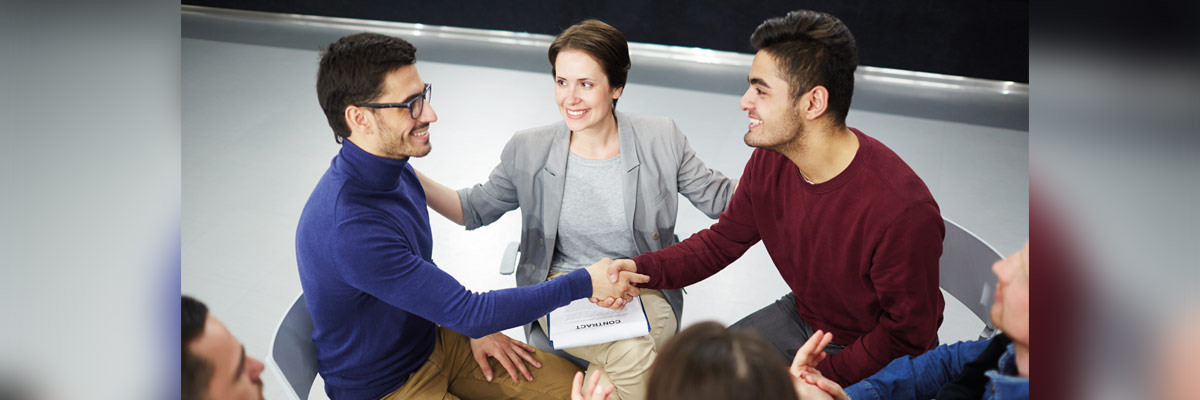 Encuentro y networking en grupo Personas sonrientes en círculo; dos hombres se estrechan la mano durante una sesión de networking y diálogo.