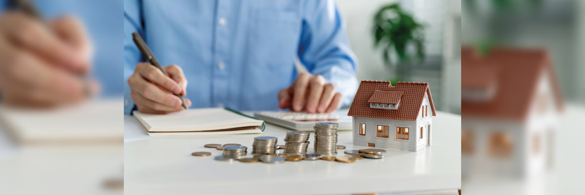 Maqueta de una casa junto a montoncitos de monedas 
