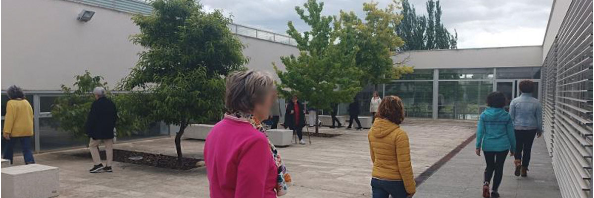 Grupo de mujeres grupo de personas caminando en un entorno exterior, que parece ser una terraza o patio. Hay árboles y bancos, y el cielo está nublado.