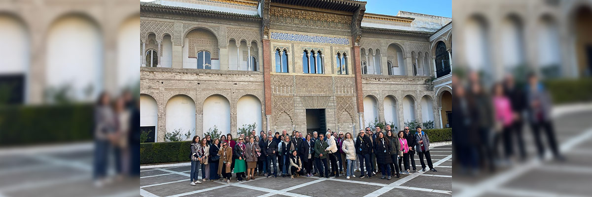 Un grupo de personas se reúne frente a un edificio histórico con arquitectura detallada, posando para una foto en una plaza pavimentada