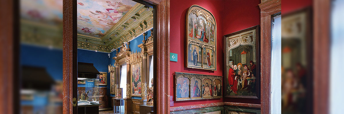 Una sala de museo con paredes rojas y azules, mostrando pinturas enmarcadas y un techo artísticamente pintado