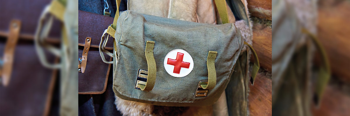 Una bolsa de primeros auxilios de estilo vintage con una cruz roja en el centro, colgada y rodeada de equipos antiguos