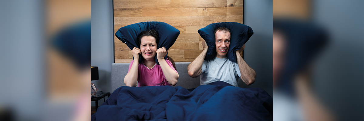 Pareja tapándose los oídos con la almohada por los ruidos molestos