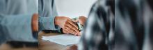 Dos personas realizan una transacción financiera, intercambiando dinero en efectivo sobre un documento, destacando el intercambio físico de moneda en acuerdos
