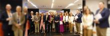 Grupo de profesionales recibiendo reconocimiento en un evento, con certificados y flores, frente a un banner que celebra el logro y la excelencia