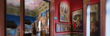 Una sala de museo con paredes rojas y azules, mostrando pinturas enmarcadas y un techo artísticamente pintado