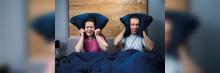 Pareja tapándose los oídos con la almohada por los ruidos molestos