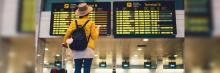 Chica con una maleta en el interior de una terminal de aeropuerto mirando las pantallas de vuelos